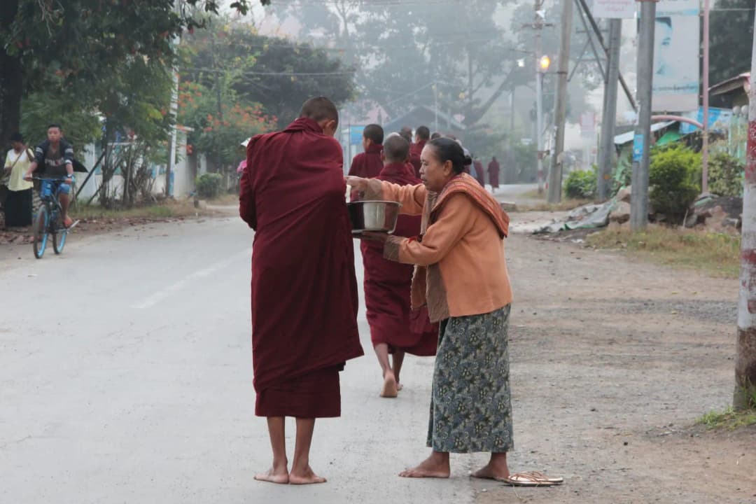 คนยืนถือถุงอาหารรอตักบาตรพระสงฆ์บนทางเท้าตอนเช้า