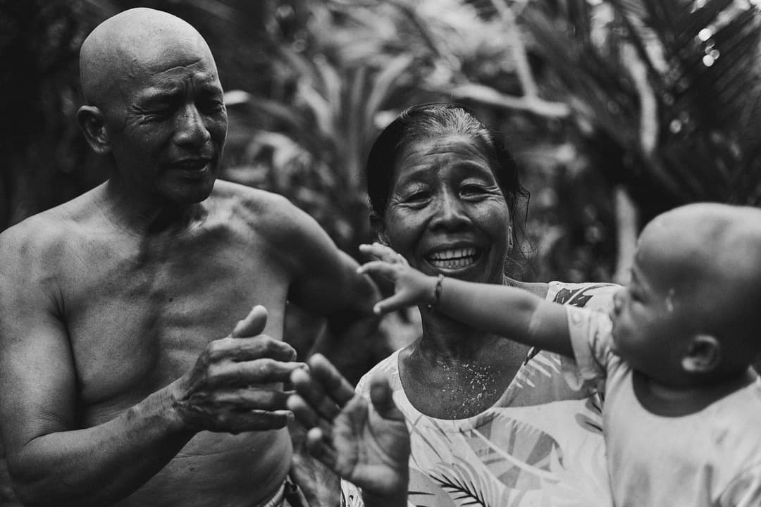 ครอบครัวสามรุ่นนั่งอยู่ด้วยกันในบ้าน ปู่ย่าตายาย พ่อแม่ และลูกน้อย