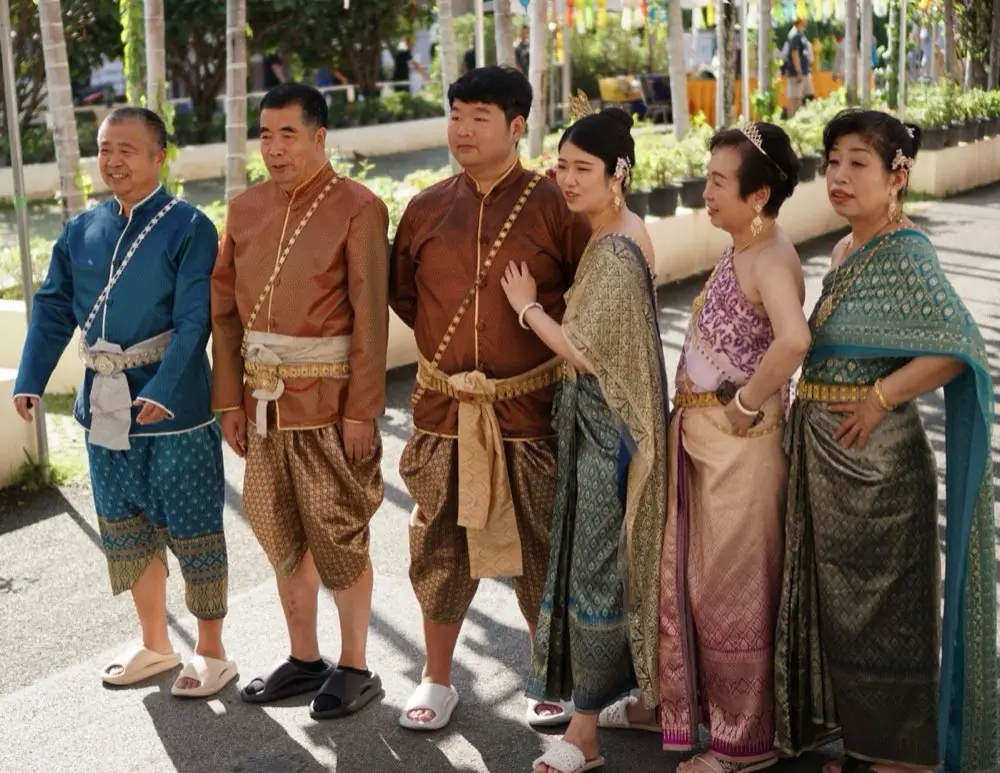 ครอบครัวไทยหลายรุ่นเดินเข้าวัดเก่าแก่ที่มีต้นไม้ใหญ่ สื่อถึงวัดประจำตระกูล