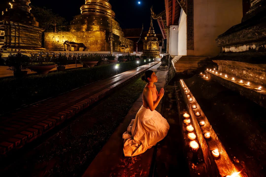 แถวพุทธศาสนิกชนถือเทียนจุดไฟเดินเวียนรอบเจดีย์สีทองในยามค่ำคืน แสงเทียนสะท้อนเป็นประกายสีทองอบอุ่น