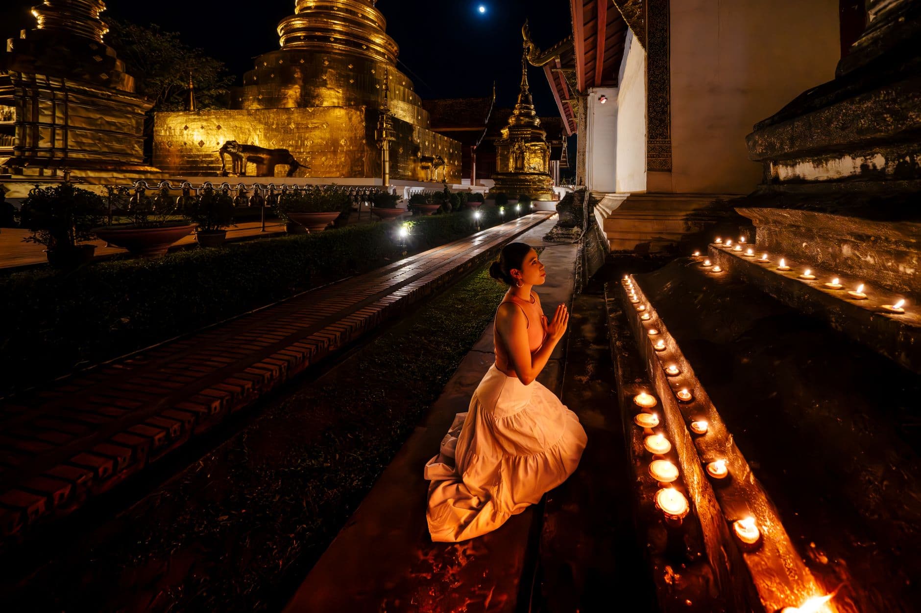 แถวพุทธศาสนิกชนถือเทียนจุดไฟเดินเวียนรอบเจดีย์สีทองในยามค่ำคืน แสงเทียนสะท้อนเป็นประกายสีทองอบอุ่น