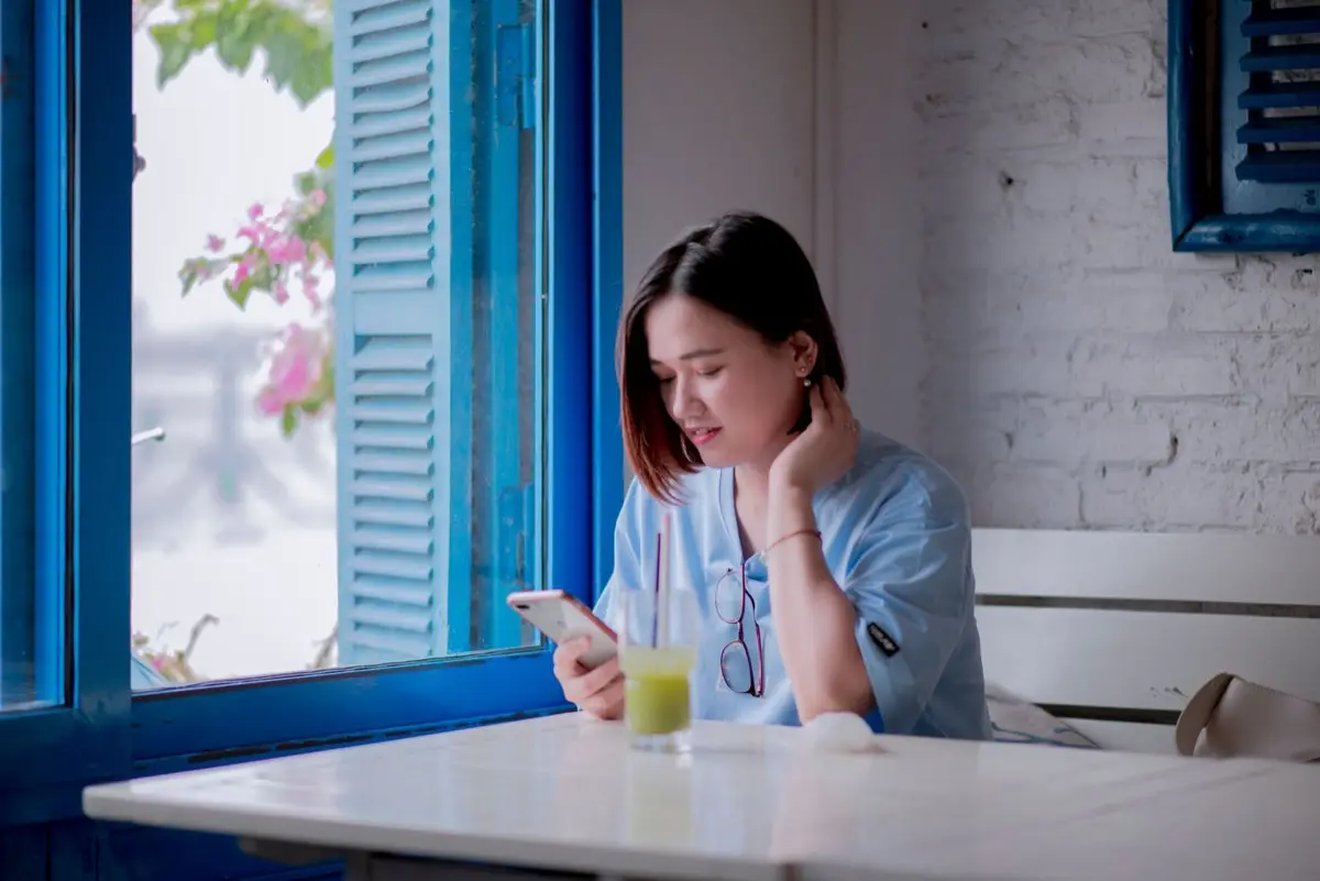 คนนั่งอ่านดวงรายวันบนมือถืออย่างผ่อนคลายระหว่างพักดื่มกาแฟ