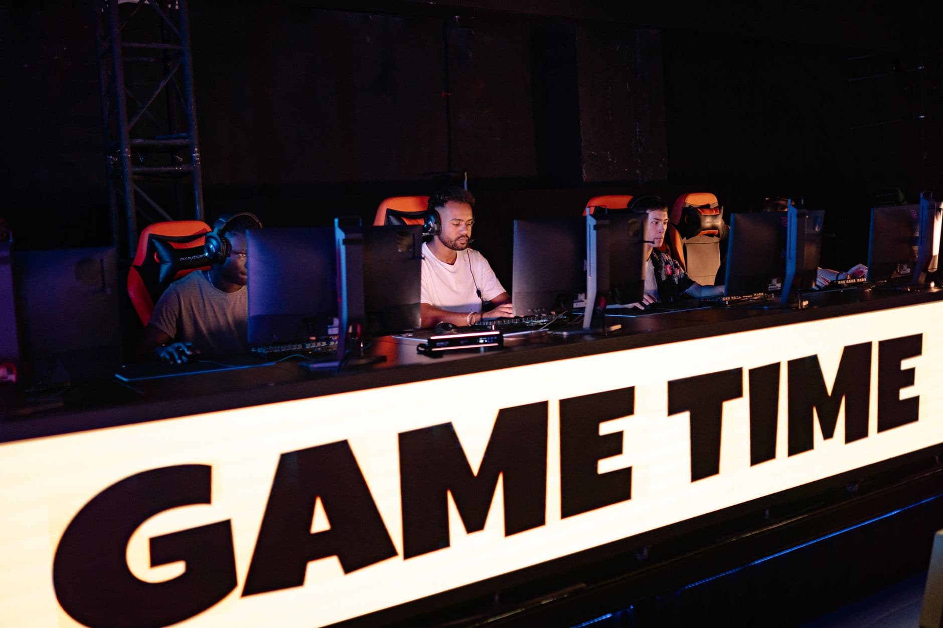 ผู้เล่นทีมอีสปอร์ตนั่งแข่งขันเกมในสนามแข่งพร้อมป้ายชื่อทีม