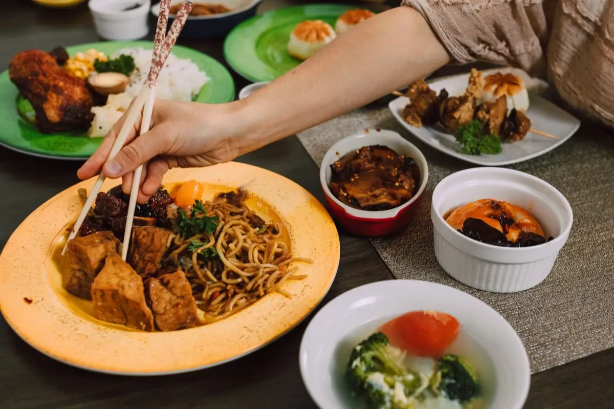 จานอาหารเจหลากสีสันวางบนโต๊ะพร้อมตะเกียบและธงเหลืองเทศกาลกินเจ