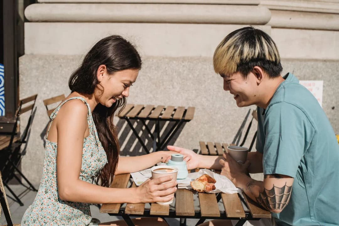 คู่รักหนุ่มสาวยิ้มพูดคุยกันระหว่างนั่งดื่มกาแฟในร้าน