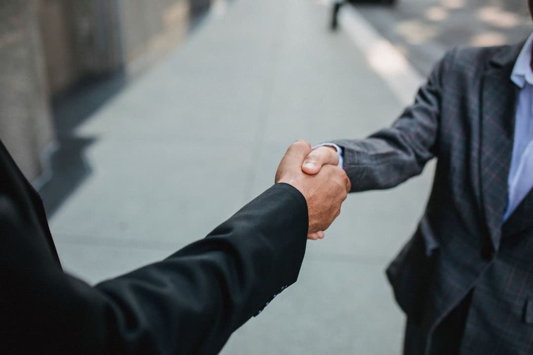 สองฝ่ายจับมือกันหลังเซ็นเอกสารสัญญาแฟรนไชส์บนโต๊ะทำงาน