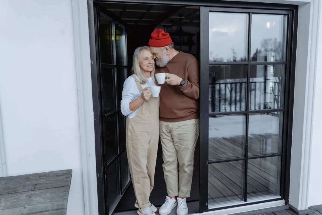 คู่รักวัยกลางคนสวมเสื้อผ้าสีเข้าชุดกันนั่งทานอาหารเย็นด้วยกันอย่างอบอุ่น
