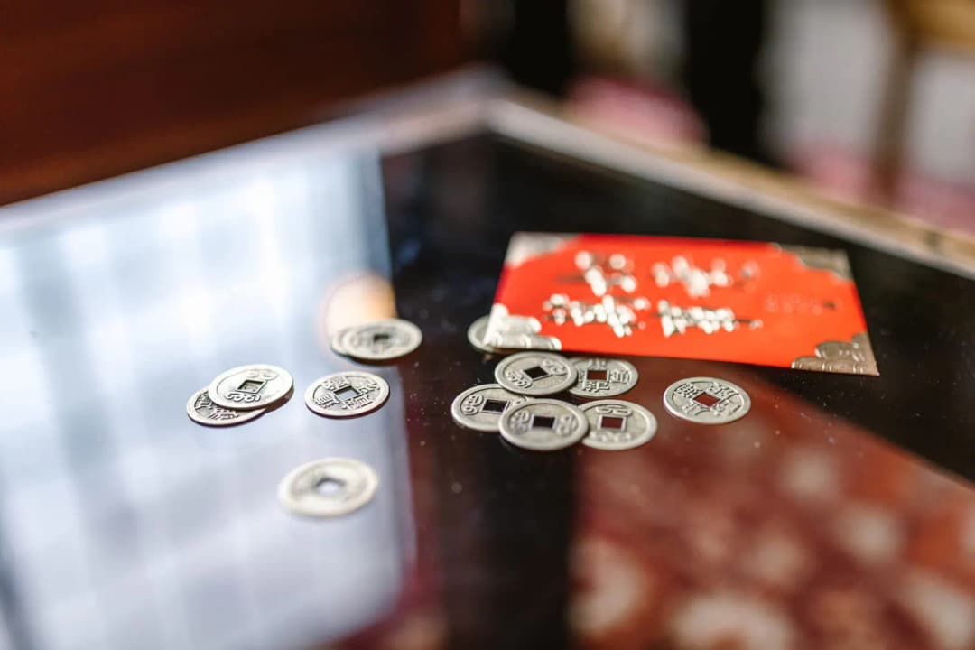 กบคาบเหรียญทองเหลืองวางอยู่บนโต๊ะไม้ใกล้เหรียญและธนบัตร
