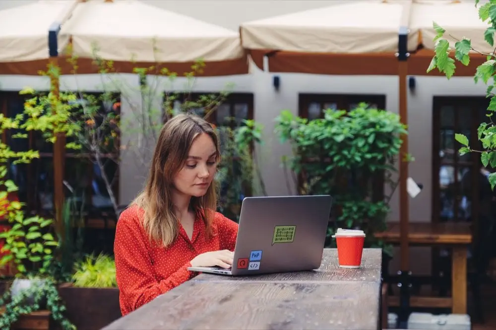 ฟรีแลนซ์นั่งทำงานกับโน้ตบุ๊กที่ร้านกาแฟ มีสมุดบันทึกรายรับรายจ่ายวางอยู่ข้างกัน