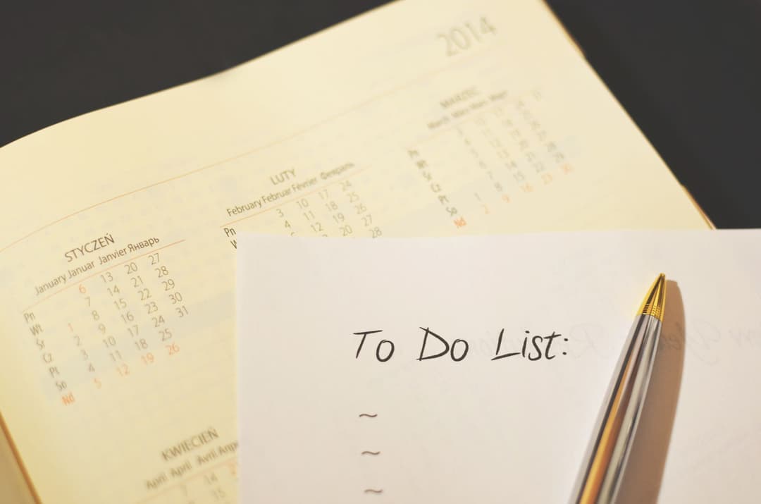 สมุดวางแผนแบบเปิดหน้าปฏิทินพร้อมกระดาษโน้ต To Do List และปากกาวางอยู่บนโต๊ะทำงาน