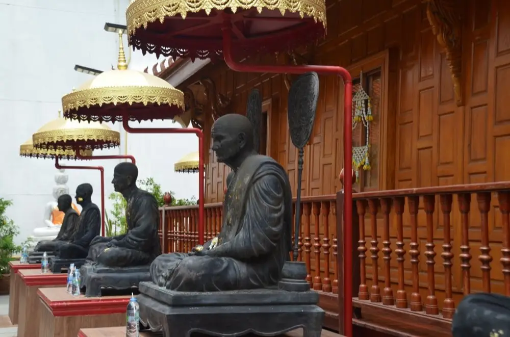 รูปเคารพพระสงฆ์หลายองค์เรียงกันบนหิ้งบูชาเพื่อเปรียบเทียบลักษณะ