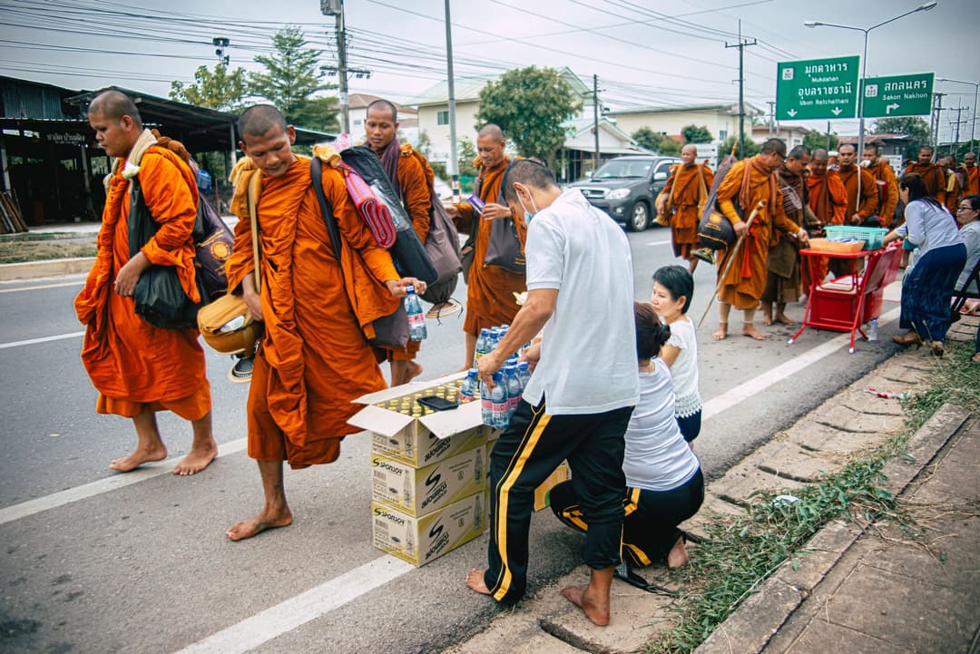 คนไทยใส่ชุดสีอ่อนตักบาตรพระสงฆ์ตอนเช้าหน้าวัด