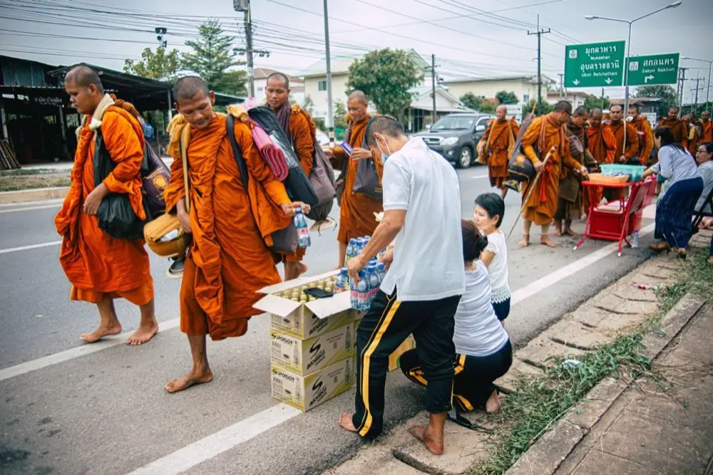 คนไทยใส่ชุดสีอ่อนตักบาตรพระสงฆ์ตอนเช้าหน้าวัด