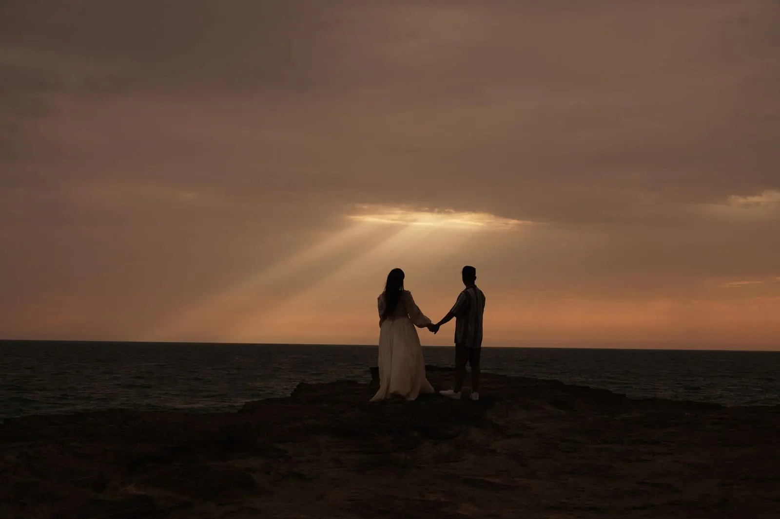 คู่รักจับมือกันเดินชายหาดยามพระอาทิตย์ตก สื่อถึงความสัมพันธ์ของคนราศีคาบเกี่ยว